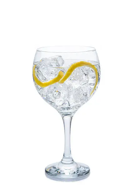 Gin and tonic in a balloon glass garnished with lemon and isolated over awhite background