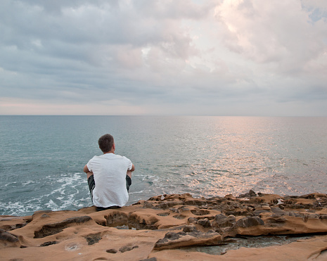 Young man sitting alone and looking at atlantic ocean sunrise, Portugal