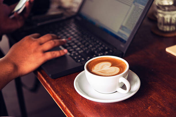 Businessman is working with laptop, holding a mobile phone in coffe shop and drinking coffe.