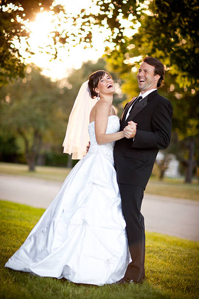 Color stock photo portrait of a happy bride and groom laughing and dancing together while backlit by the sun outside.