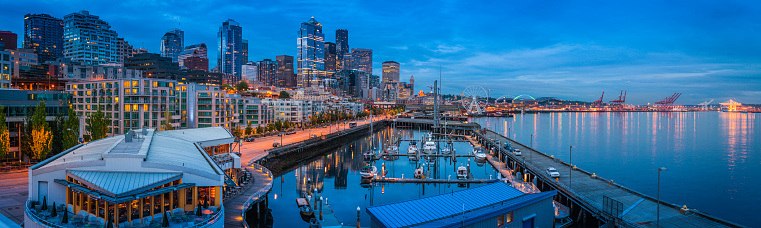 Panoramic vista over the night lights and crowded cityscape of the Seattle waterfront, from the marina and luxury condominiums past the soaring skyscrapers of downtown to the aquarium, ferry docks and the illuminated cargo cranes of the massive container port on Puget Sound, Washington, USA. ProPhoto RGB profile for maximum color fidelity and gamut.