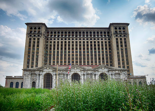 Michigan Central Station With Weeds Detroit, USA - June 9, 2015: A view of the front facade of the Michigan Central Railway Station as seen over weeds growing in front of the building. The historic landmark is in disrepair. detroit ruins stock pictures, royalty-free photos & images
