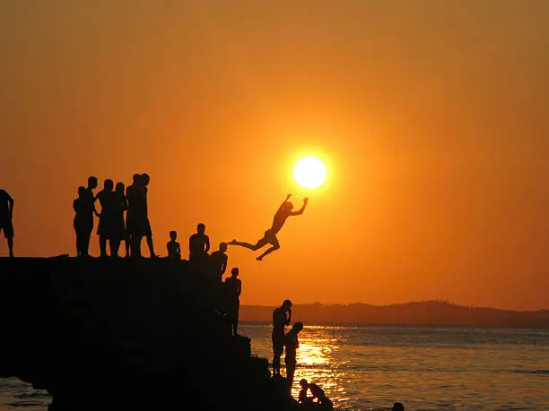 Boys jumping from the se wall at sunset on Porto da Barra beach, Salvador, Brazi