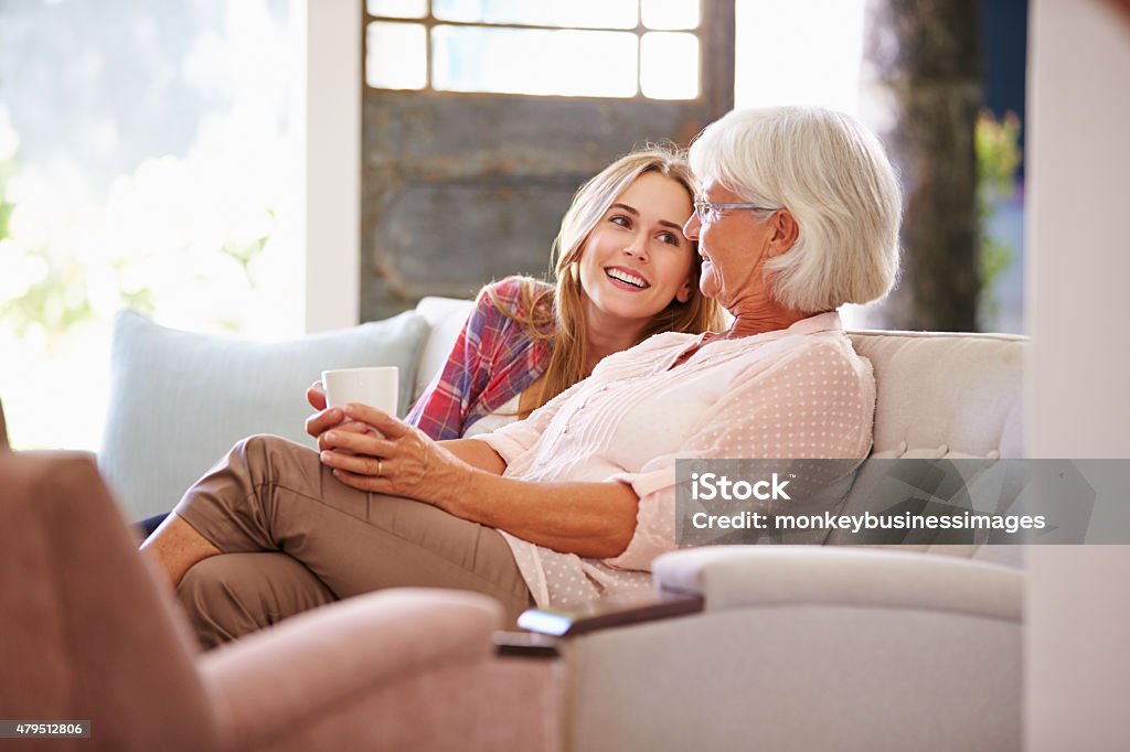 Grandmother With Adult Granddaughter Relaxing On Sofa Grandmother Stock Photo