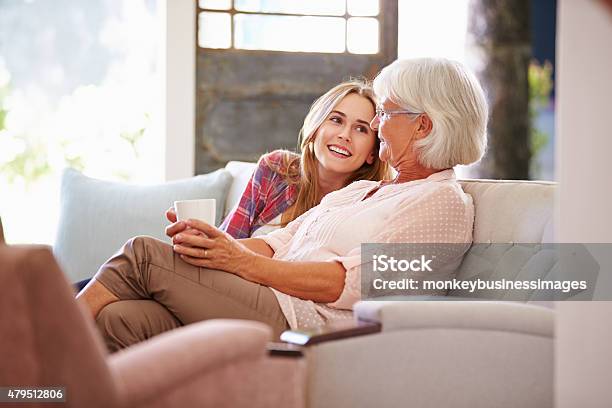 Grandmother With Adult Granddaughter Relaxing On Sofa Stock Photo - Download Image Now