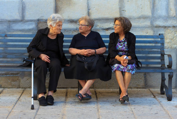 Ragusa Ibla (Sicily), Italy - June 14, 2015: Three senior women--two wearing black and one with a cane--chat on a bench in Southeast Sicily, Italy.