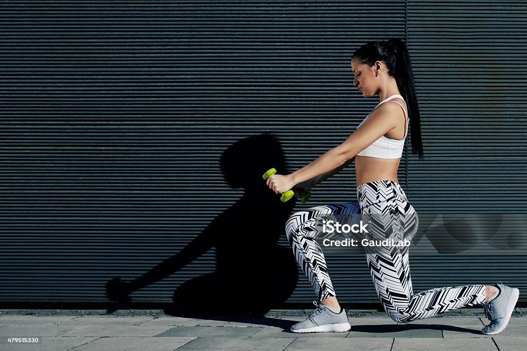 Girl with strong body and perfect figure exercising with dumbbells Young fit woman with strong body and perfect figure exercising with dumbbells outside on black wall background, athletic female toning with weights standing against copy space for your text message 2015 Stock Photo