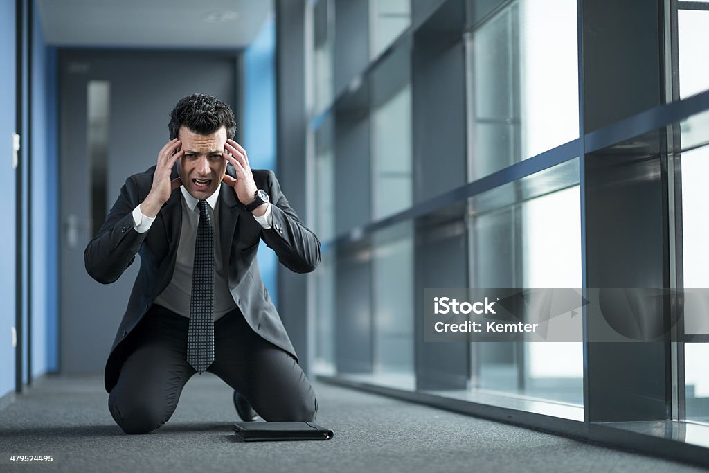 businessman with headache kneeling at floor horrified businessman kneeling on the floor of a modern office building holding his head 30-39 Years Stock Photo