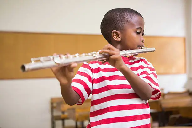 Photo of Cute pupil playing flute in classroom