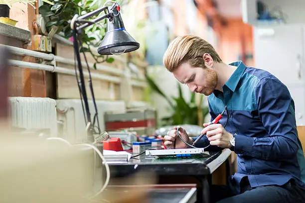 Photo of Young handsome man soldering a circuit board