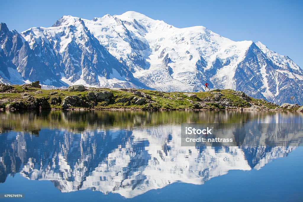Reflection on crystal clear alpine lake, running man A trail runner in red runs along a crystal clear lake with the majestic Mont Blanc in the background. An almost perfect reflection is shown in the water of the lake. Mont Blanc Stock Photo