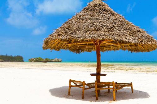 Isolated Wooden parasol and beach chairs in Zanzibar with little island on background