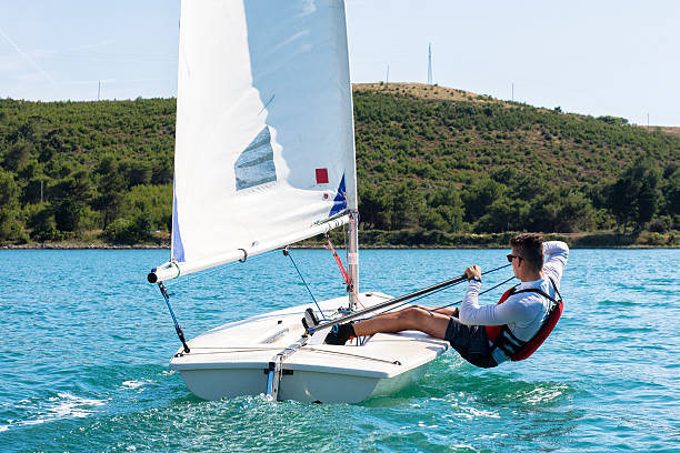 Young man sails a laser class sailing boat International laser class sailing boat with young male boats-man practicing, side view sailing dinghy stock pictures, royalty-free photos & images