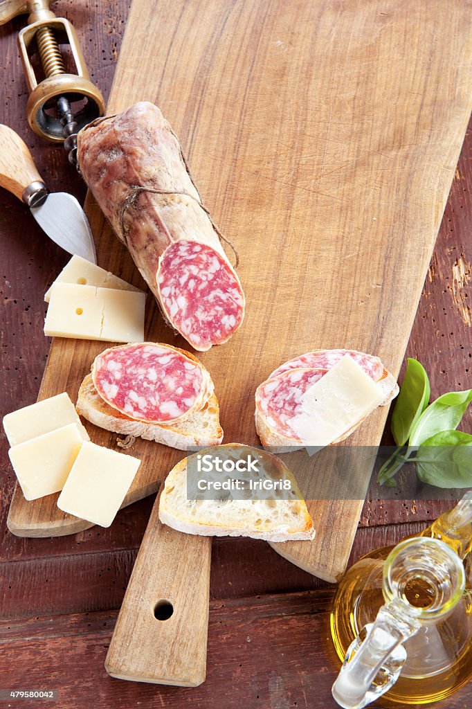 cheese and salami on wooder background two wineglass with red wine and assortment of cheese and salami. olive oil & basil 2015 Stock Photo