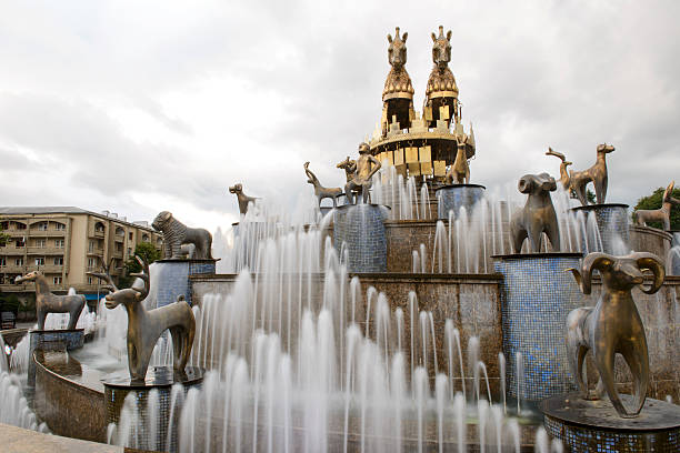 Kutaisi, Georgia - May 5, 2013: Detail from the central square in Kutiasi. People are looking at water fountain, taking pictures or sitting on its edge. In centre is fountain while in background are some buildings and trees from park. Above everything is blue sky.