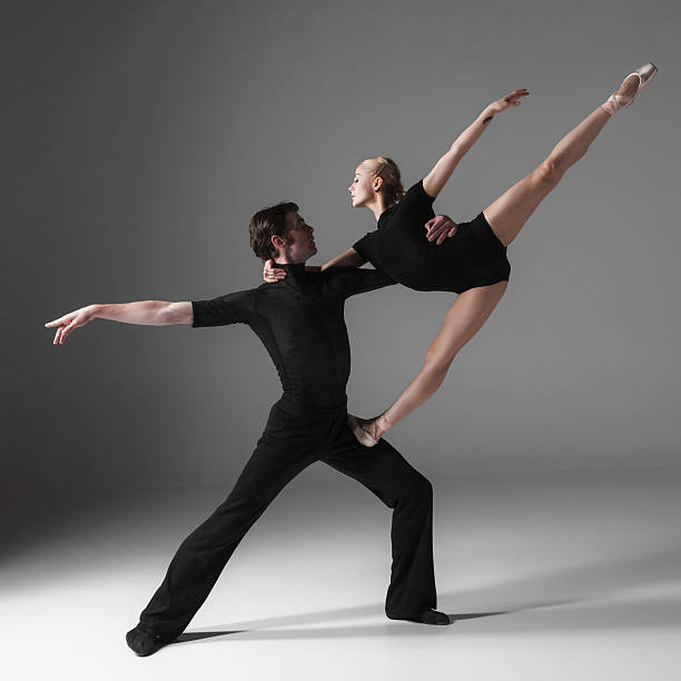 The two young modern ballet dancers in black suits posing over gray studio background 