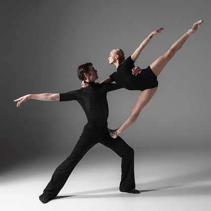 The two young modern ballet dancers in black suits posing over gray studio background 