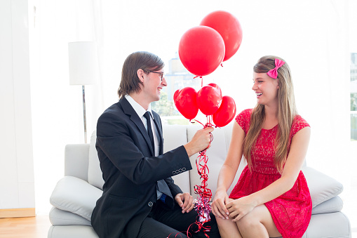 Cute geeky couple with red balloons on the couch