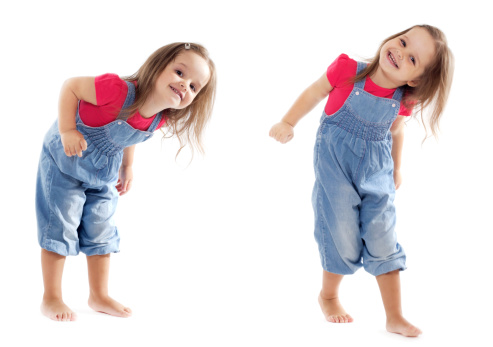 Happy toddler girl wearing jeans jumpsuit is having a great time dancing in the studio. Isolated on white..