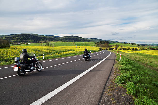 las motocicletas que viaje por una carretera vacía entre florecer la violación campos - fossil fuel biology oilseed rape agriculture fotografías e imágenes de stock