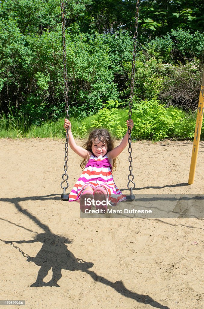 Litlle girl on a swing A little girl having fun on a swing in a park during a nice day of summer. She wears a dress and smiles Child Stock Photo