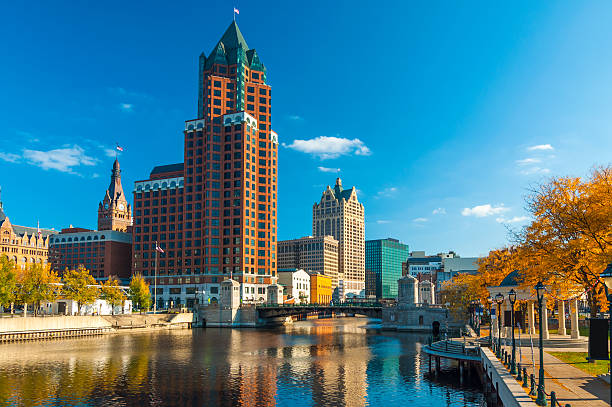 Downtown Milwaukee skyscrapers (prominently showing Milwaukee Center) with the Milwaukee River and orange colored trees during Autumn in the foreground.