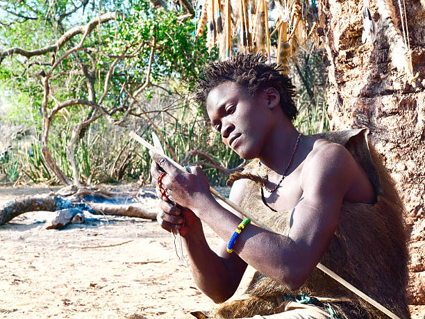 Hadzabe (or Hadza) young bushman making the arrow for a hunting bow. The Hadzabe are an indigenous ethnic group in north-central Tanzania, living around Lake Eyasi in the central Rift Valley and in the neighboring Serengeti Plateau. The population of Hadza tribe just under 1000 persons. Endangered tribe. They are among the last hunter-gatherers in the world.