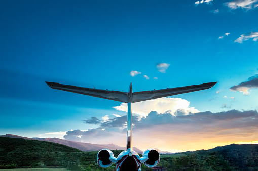 Tail and engines of a private luxury jet in the mountains of Colorado near Aspen at sunset with a dramatic cloudscape on the horizon.