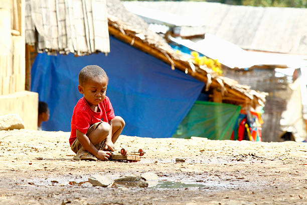 small African boy , outdoors, playing with a car made out of wood