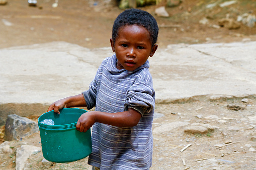 Poor malagasy boy carrying plastic water bucket - poverty