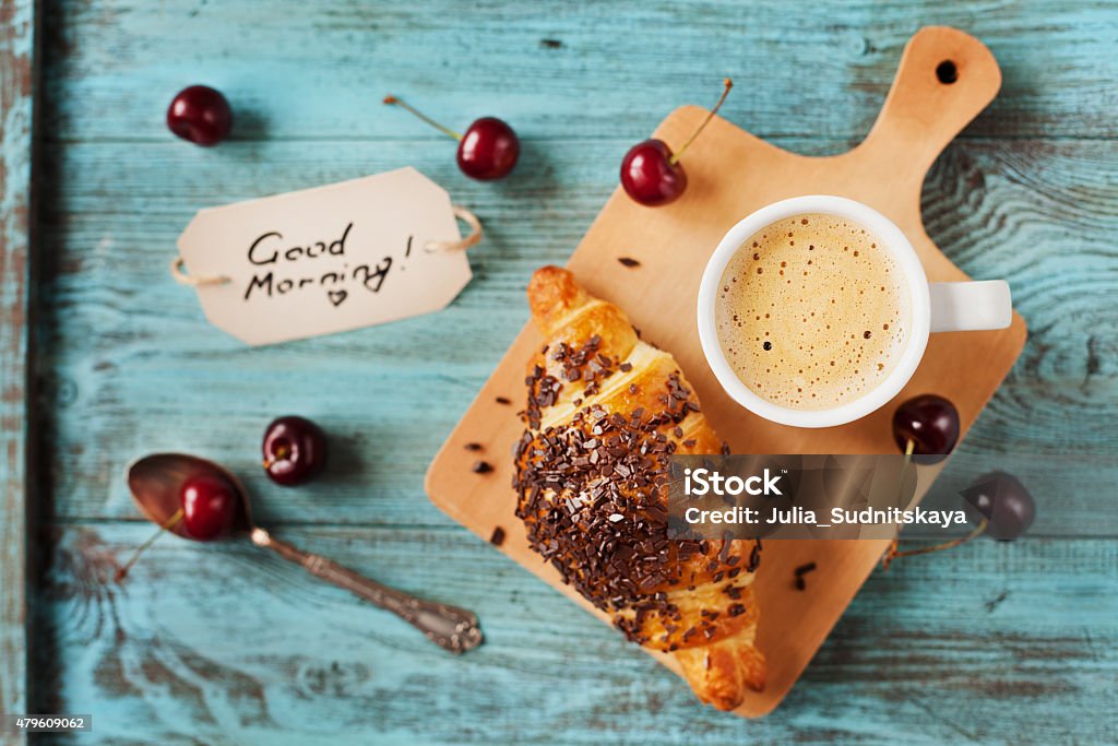 breakfast with fresh croissant, coffee, cherries and note Tasty breakfast with fresh croissant, coffee, cherries and notes on a wooden table, selective focus on coffee 2015 Stock Photo