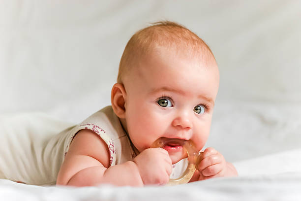 Baby girl on her stomach with teether in the mouth Six-month baby girl on her stomach with teether in the mouth 6 11 months stock pictures, royalty-free photos & images
