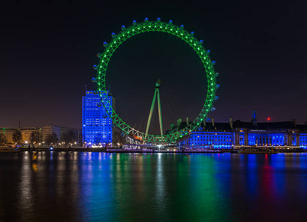 The St Patrick Day London Eye London, United Kingdom - March 16, 2014: A long exposure night shot of the London Eye with the St Patrick Day green color and the Shell building along the Thames. london county hall stock pictures, royalty-free photos & images