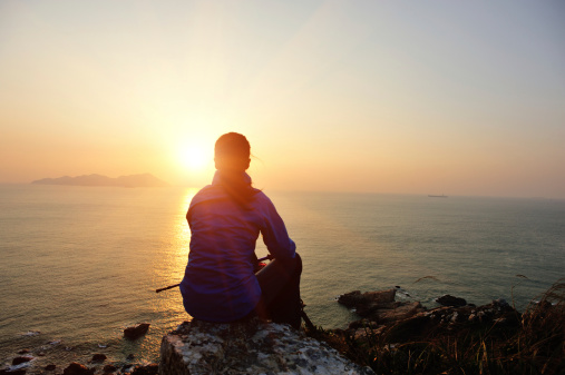 woman hiker sit on rock face the sunrise at seaside