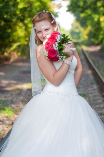 beautiful young the bride with a bouquet of red-white roses on a track in the summer