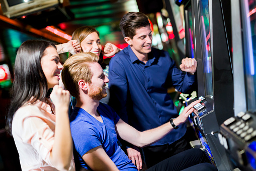 Young group of people gambling in a casino playing slot and various machines
