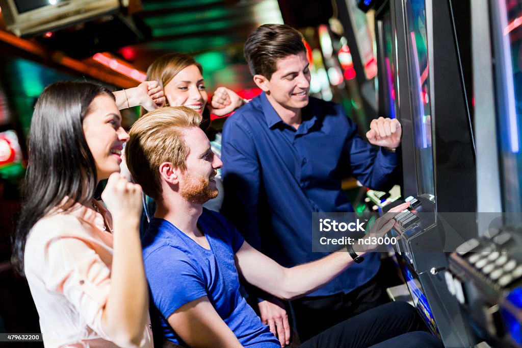 Friends gambling in a casino playing slot and various machines Young group of people gambling in a casino playing slot and various machines Amusement Arcade Stock Photo