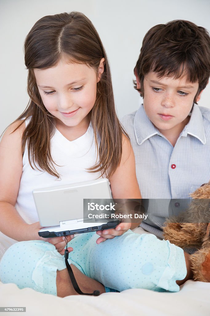 a boy watching girl play a handheld game  60-64 Years Stock Photo