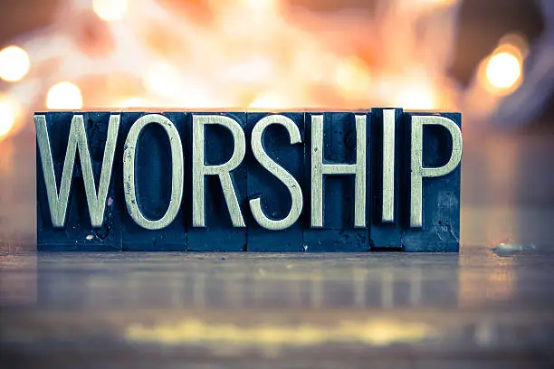 The word WORSHIP written in vintage metal letterpress type on a soft backlit background.