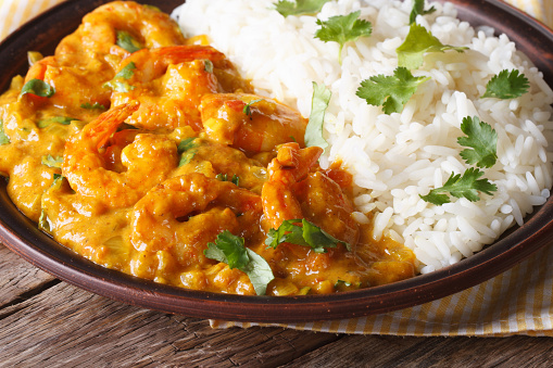 Shrimps in curry sauce with rice and cilantro closeup on a plate. horizontal