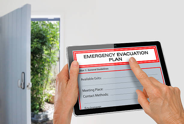 Hands using Tablet with Emergency Evacuation Plan beside Exit Door stock photo