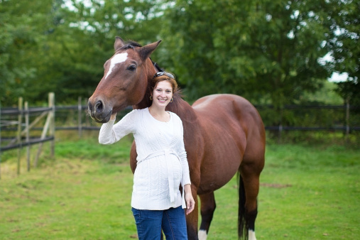 Attractive young pregnant woman and a horse standing in a field in autumn