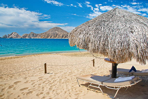 Cabo San Lucas beach Beach location with chaise and umbrella for relaxation in Cabo San Lucas, Mexico with mountains in view across the water. cabo san lucas stock pictures, royalty-free photos & images