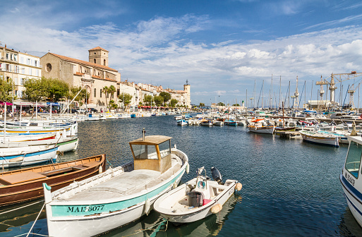 La Ciotat, France - August 20, 2014: Port of La Ciotat  (French Riviera). Many boats (fishing boats and sailing boats) on interna bay of the Port. in background some people walking on promenade near bars and restaurants. On the left in background the Notre Dame de l'Assomption.