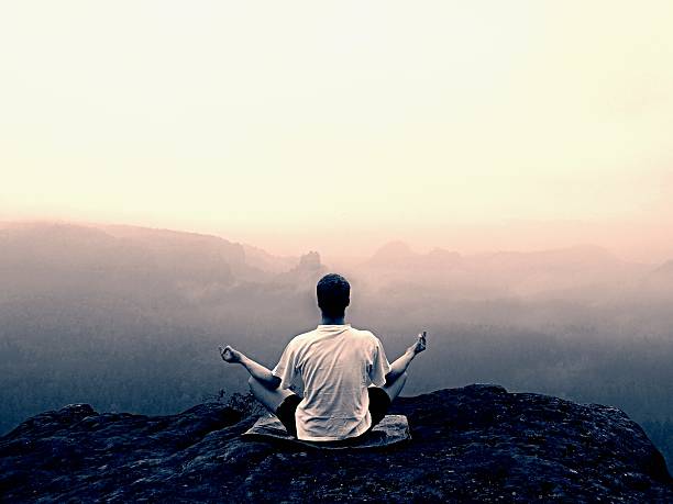 istock Man do Yoga pose on rocks peak within misty morning 479690050