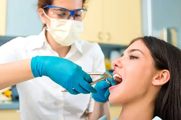 A dentist is using dental pliers to extract a tooth from a female patient.