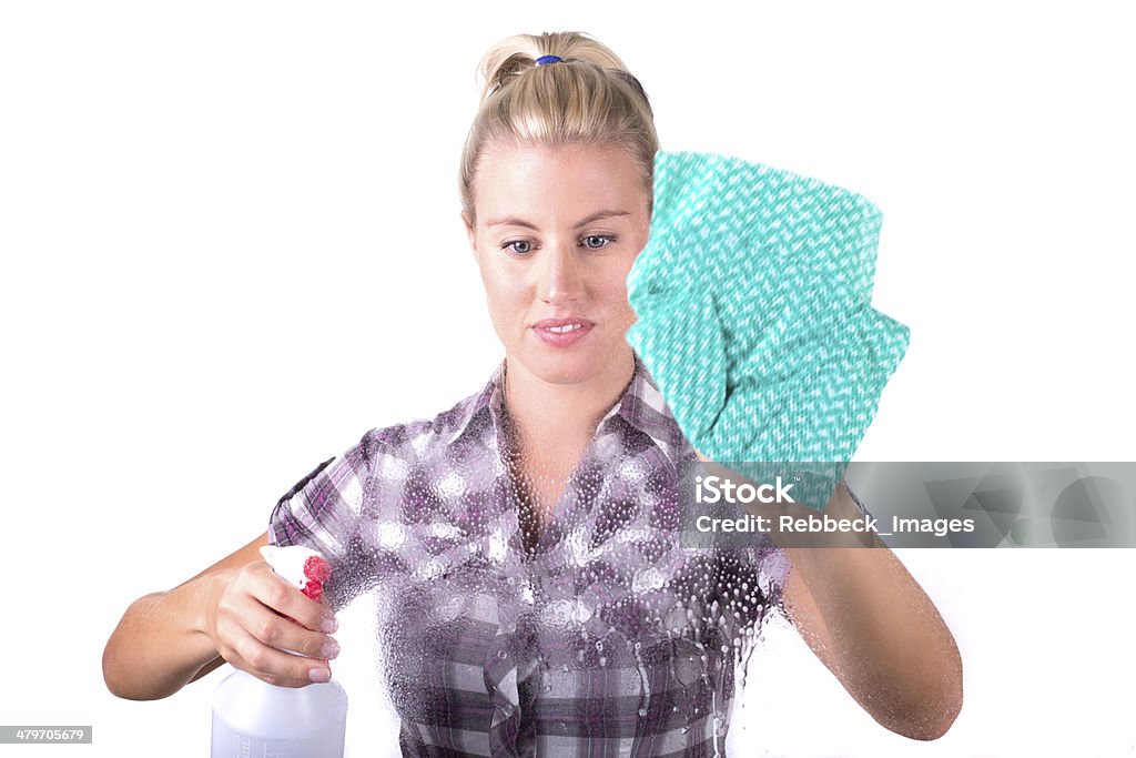 Window cleaning A young woman sprays a cleaning agent on a window and uses a cloth.  She has blonde hair and is wearing a checked shirt 20-24 Years Stock Photo