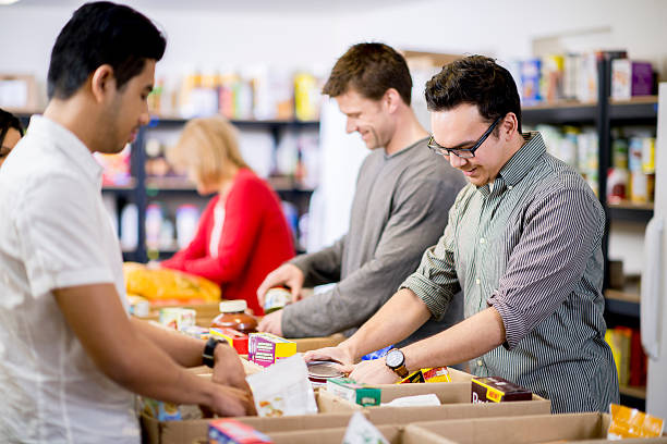 Community Service Young adults at a community service food bank, preparing boxes with food donations. soup kitchen stock pictures, royalty-free photos & images