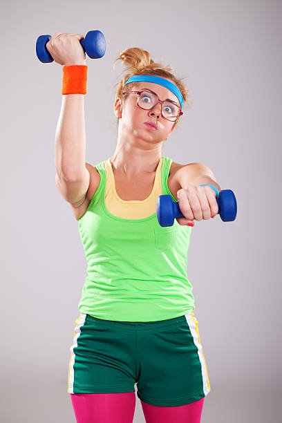 Nerd fitness girl wearing glasses exercising with small weights Young nerd fitness girl working out. Funny blonde woman with glasses exercising with small weights and looking tired. She is wearing sports clothing.Behind her is gray background with vignette. Image is made in photo studio with DSLR camera. nerd lifting weights stock pictures, royalty-free photos & images