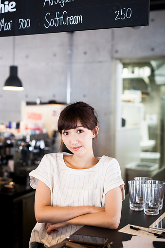 Young asian waitress is leaning on a bar counter and smiling generously. Photo contains copy space.